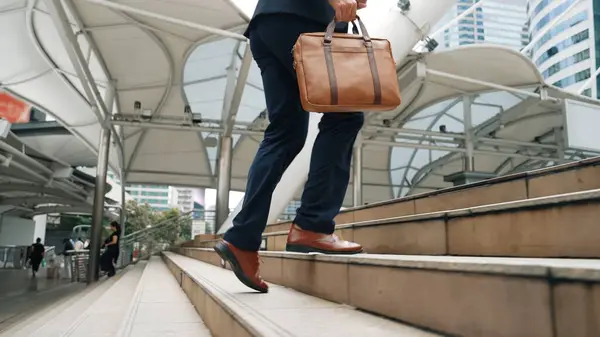 Close up of businessman leg walking up stairs surrounded by urban view. Back view of ambitious project manager finding challenging job or investment opportunity at city with modern building. Urbane.