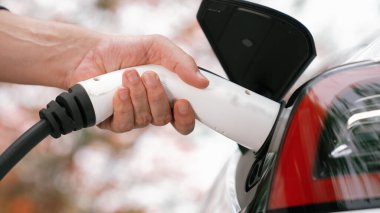 Temiz ve sürdürülebilir enerji kullanarak şarj istasyonundan şarj olmak için EV şarj cihazını EV vagonuna takın. Doğal koruma ve çevre dostu araba yolculuğu konsepti. Yükselt