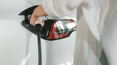 Genç hareketli kadın, EV elektrikli arabasıyla şehir merkezindeki alışveriş merkezinin otoparkına gidiyor. Sürdürülebilirlik yaşam tarzını yeşil, temiz, yeniden şarj edilebilir elektrikli araç iç organlarıyla şarj ediyor.