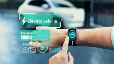İş adamı, istasyonun otoparkından şarj olurken akıllı telefon hologramındaki EV aküsünün durumunu kontrol ediyor. EV teknolojisi adaptasyonu için temiz enerjinin gelecekteki yaşam tarzı. İnceleyin
