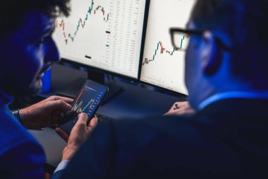 İki borsa simsarı akıllı telefon ve dinamik dijital para birimi dizüstü bilgisayar sunucusu verilerini araştırıyor. Yatırımcılar, işyerinin dekoratif neon mavi ışığındaki pazar hisselerini analiz ediyorlar. Satılabilir.