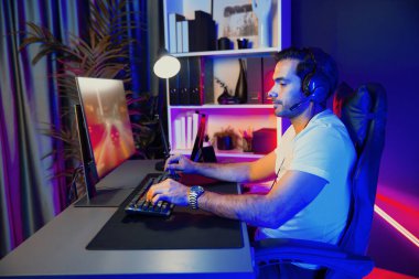 Kulaklık takan akıllı oyun flaması hafta sonu neon dijital siber ışıklandırma odasında son yaşam tarzı yarışmasında şampiyon olmak için bilgisayar ekranında araba yarışı oynamaktan zevk alır. Tahmin et..