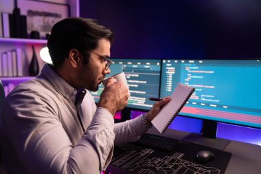 Akıllı bilişim geliştiricisi, bilgisayar ekranındaki yazılım geliştirme kodlaması üzerine kahveyle birlikte çalışıyor, en yeni uygulama projesi programı ile birlikte neon ışıklı siber ofiste çevrimiçi web sitesi verilerini güncelliyor. Tahmin et..