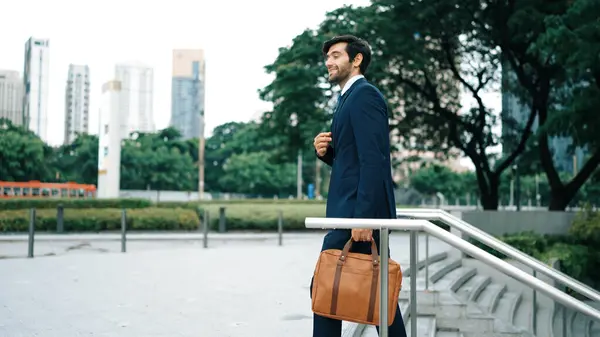 Skilled business man walking up stairs at park or city while holding bag in the hand Professional project manager going to workplace. Represent growth, getting promotion, increasing skill. Exultant.