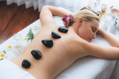 Lüks tatil köyündeki kaplıcalarda sıcak taş masajı. Gün ışığı sükunet ortamında, mutlu kadın müşteri bazalt taş masajından zevk alıyor. Rahatlatıcı bir sıcaklıkla vücudun üzerinde süzülüyor. Sessiz.