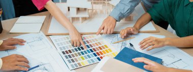 Yetenekli mimar takımı ev inşaatı hakkında tartışırken, iç mimar ev modeli ve bina planının dağıldığı renk paletine uygun bir renk belirliyor. Üst Manzara. Değiştirilmiş.