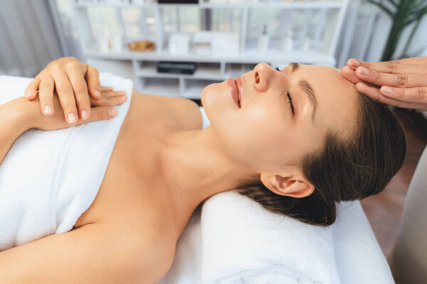 Caucasian woman enjoying relaxing anti-stress head massage and pampering facial beauty skin recreation leisure in dayspa modern light ambient at luxury resort or hotel spa salon. Quiescent