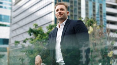 Kafkasyalı iş adamı cep telefonunu tutuyor ve gökdelen manzarasına bakıyor. Modern binanın çatısında duran yetenekli erkek lider. Kafkasyalı yönetici gözlerini dinlendirirken telefona bakar. Urbane.