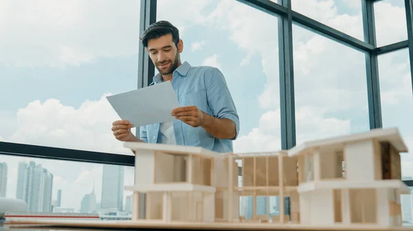 Professional architect engineer reading blueprint while inspect house model. Manager or businessman looking at architectural document while looking and smiling at camera. Closeup. Tracery