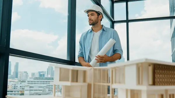 Smart civil engineer standing, walking while looking at house model and architectural equipment. Engineer with safety helmet standing near city view while standing near building model. Tracery