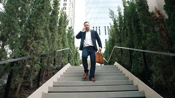 Happy businessman walking down stair and calling manager by using smart phone. Top view of manager talking marketing team and planning financial strategy by telephone while going down stair. Urbane.