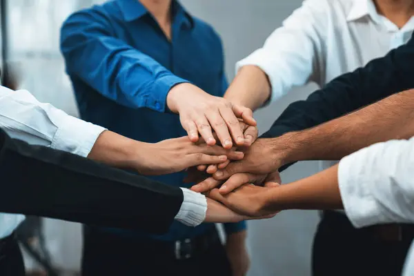 Group of diverse office worker join hand together in office room symbolize business synergy and strong productive teamwork in workplace. Cooperation and unity between business employee. Prudent