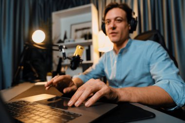 Sunucu kanalı akıllı yayıncı laptopta canlı sosyal medya uygulaması arıyor, kulaklık takıyor ve modern ofis stüdyosundaki mikrofonu kullanıyor. Bireysel.