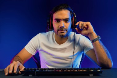 Akıllı oyun flaması kameraya modaya uygun şekilde bakıyor, bilgisayar üzerinden online oyun kullanıcısı seviyesini geçiyor, dijital neon ışıklı stüdyo odasındaki diğer insanlarla iletişim kurmak için kulaklık ve mikrofon kullanıyor. Tahmin et..