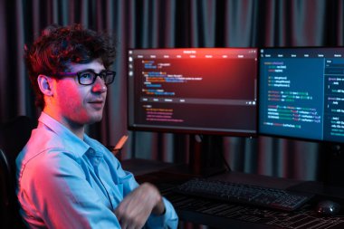 Ekranda yazılım geliştirme bilgisine karşı oturan gülümseyen bilişim geliştiricisinin profili, web sitesindeki son sürüm uygulaması için program kodlaması oluşturarak çevrili kameraya bakıyor. Toplayıcı.