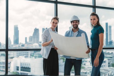 Bir grup zeki mimar proje planlarını tutarken kameraya bakıyor. Kaliteli yönetici takımı inşaat hakkında konuşurken şehir manzaralı bir yerde duruyor. Ekip çalışıyor. İzleme.