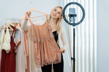 Genç sosyal medyum kadın moda videosu yapıyor. Blogcu kameraya ve ışık çemberine gülümserken, aynı zamanda ikna edici çevrimiçi kıyafetleri izleyicilere veya takipçilere vlog sattırıyor. Blithe