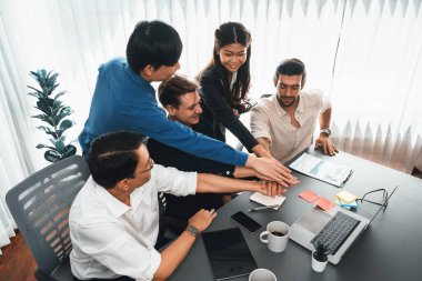 Çeşitli ofis çalışanlarından oluşan bir grup, ofis odasında el ele vererek iş sinerjisini ve iş yerindeki güçlü verimli takım çalışmasını sembolize ediyor. İş çalışanları arasındaki işbirliği ve birlik. Tedbirli