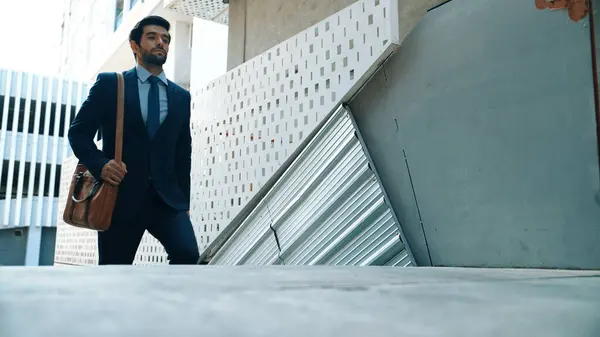 Smart business man walking up the stairs with confident near building. Skilled project manger walking on stairs seeking for job, going for new job near at modern skyscraper. Copy space. Exultant.