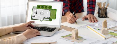 Profesyonel mimar, modern ofise yerleştirilen ahşap blok, plan ve mimari belge ile karışık masa üzerinde proje yöneticisi olarak dizüstü bilgisayarda sergilenen ECO evini temsil ediyordu. Kapatın. Tanımlama.