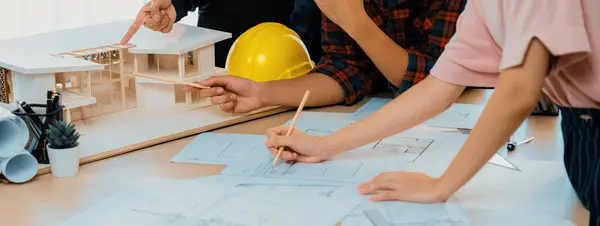Cropped image of professional architect engineer team meeting analysis house model construction while coworker draws blueprint at meeting table with architectural document and house model. Burgeoning.