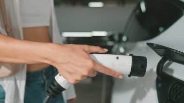 Genç hareketli kadın, EV elektrikli arabasıyla şehir merkezindeki alışveriş merkezinin otoparkına gidiyor. Sürdürülebilirlik yaşam tarzını yeşil, temiz, yeniden şarj edilebilir elektrikli araç iç organlarıyla şarj ediyor.