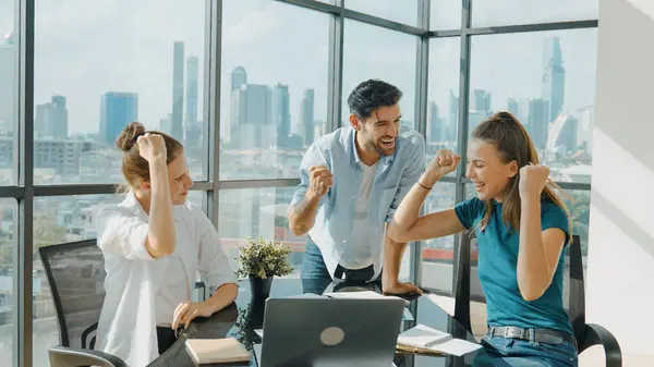 Professional business team receive a good news by using laptop while celebrate their success. Project manager high five and clap hands in front of laptop with colleague at modern office. Tracery