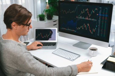 Bilgisayar ve dizüstü bilgisayarı kullanarak, çalışma masasındaki dinamik artırılmış borsa grafiğinin en yüksek kar değerini araştıran bir tüccar, modern ofisteki ekrandaki döviz kuru değerini analiz ediyor. Bireysel.