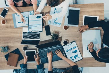 Modern ofisteki iş adamları ve iş kadınlarıyla grup toplantısındaki iş adamlarının en üst düzey görüşü, masada dizüstü bilgisayar, kahve ve belge ile. Kurumsal şirketler uds