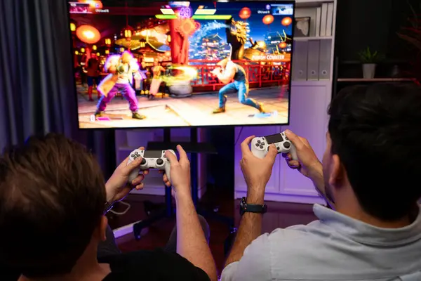 Friend gamers playing video game of battle martial arts fighter on TV using joysticks position of backside background. Comfy living neon light at home place with cheerful fighting winner. Sellable.