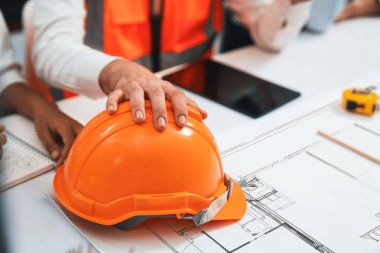 Mimari proje üzerinde birlikte çalışan çeşitli inşaat mühendisi ve müvekkil grupları, inşaat planını gözden geçirip toplantı masasında plan oluşturuyorlar. Tedbirli