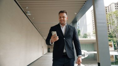 Happy proje yöneticisi koridorda yürürken cep telefonunu kontrol ediyor. Profesyonel iş adamı başarılı projesini kutlarken ya da satışları artırırken takım elbise giyer ve bavulu toplantı için tutar. Urbane.