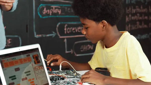 アフリカの少年は 電子ツールを使用することを学んでいますが ラップトップのディスプレイエンジニアリングコードや Stemテクノロジークラスで書かれたWeb開発計画をブラックボードの前に座っている間 イスラーム主義 — ストック写真