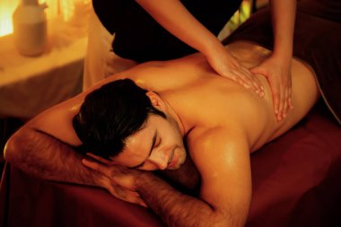 Beyaz erkek müşteri stres önleyici spa masajının keyfini çıkarıyor ve lüks otel ya da oteldeki ortam kaplıcalarında sıcak mum ışığında güzellik teniyle eğleniyor. Sessiz.