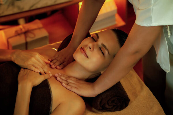 Caucasian woman customer enjoying relaxing anti-stress spa massage and pampering with beauty skin recreation leisure in warm candle lighting ambient salon spa at luxury resort or hotel. Quiescent