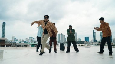 Profesyonel break dans takımı çatıda çok kültürlü arkadaşlar varken break dans alıştırması yapıyor. Genç modern dans grubu hip hop hareketi yapıyor. Tarz, moda, aksiyon. Açık hava sporu 2024. ÇalışmaComment.
