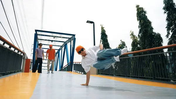 全景拍摄专业嬉皮士表演B男孩的表现和精力充沛的脚步声 有技巧的快乐人在桥边练习霹雳舞 而朋友则在桥边为他欢呼 2024年户外运动 神气活现 — 图库照片