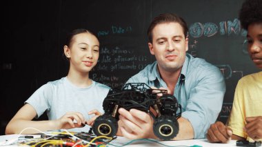 Akıllı öğretmen araba modelini farklı öğrencilere denetliyor. Karışık ırk dinleyicisi olan liseli çocuklar masadaki dizüstü bilgisayarlı ve kablolu robot model sistemini açıklıyor. Öğretim.