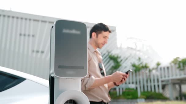 慢动作男子使用智能手机支付电费的公共电动车收费站在城市商业购物中心停车场 利用越野车的现代环境和可持续城市生活方式 — 图库视频影像