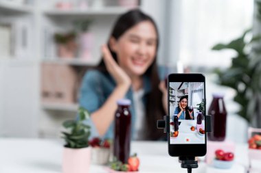 Seçici odaklı akıllı telefon ve gülümseyen genç, güzel Asyalı karışık çilek ve kiraz suyu detoksu değerlendirmesi sosyal medyada sağlıklı ürün tanıtımı sunuyor. Taktik.