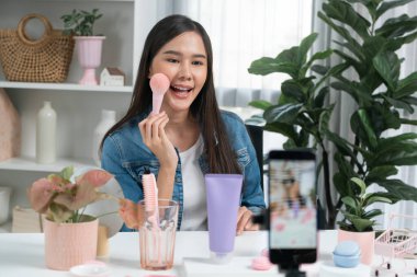 Genç, güzel Asyalı makyaj fırçası yanak testi koleksiyonunu pastel renkle inceliyor. Sosyal medyada akıllı telefonu tanıtmak için pembe ile ışıltılı bir ruh hali sergiliyor. Taktik.