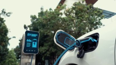 Doğal yeşil araba parkındaki ekolojik temiz enerji şarj istasyonundan gelen fütürist akıllı EV şarj aletinin şarj ettiği elektrikli araba. Alternatif enerji kullanan gelecekçi çevre dostu elektrikli araba. İnceleyin