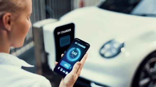 スマートEvモバイルアプリによるスマートフォンディスプレイのバッテリーステータスインターフェースを持つビジネスマンや 駐車場の充電ステーションから電気を充電する環境に優しいEvカー Peruse — ストック動画