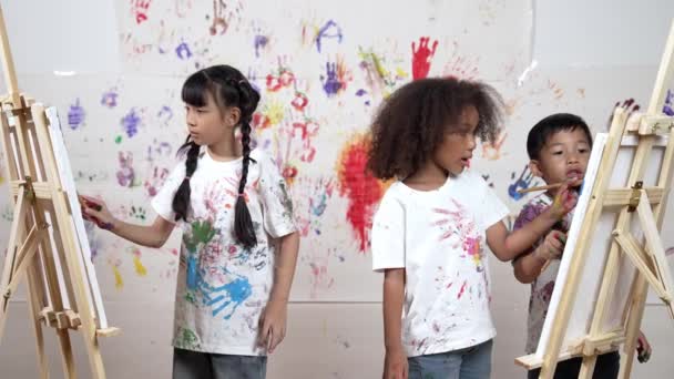 多様な学生がアートレッスンでステンドウォールで絵を描いたり キャンバスを描いたりします アジアの少女は 手のプリントでステンドウォールに立っている間 染色された色の白いシャツを着ています クリエイティブ活動 エラー — ストック動画