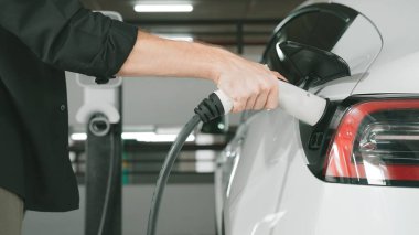 Genç adam EV elektrikli arabasıyla şehir merkezindeki alışveriş merkezinin otoparkına gidiyor şehir merkezindeki sürdürülebilirlik yaşam tarzını yeşil, temiz, yeniden şarj edilebilir elektrikli araç iç organlarıyla şarj ediyor.