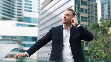 Erkek liderin etrafını sarın kulaklığı dinleyin ve neşeli ve motive edici bir şekilde rahatlatıcı müzikle dans edin. Becerikli proje yöneticisi şehir merkezinde akıllı telefon kullanırken rahat şarkılar dinlemeyi sever. Urbane.