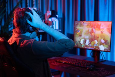Stresli genç oyun flamasının sunucu kanalı Moba 'yla savaş meydanında yenilgiye uğrayan çoklu oyun takımını kırmızı neon odadaki arka yüzü görüntülü bir kulaklık takarak yeniyor. Toplayıcı.
