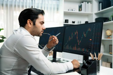 Akıllı tüccar işadamı, modern merkez ofisindeki araştırma pazarında en yüksek kârlı finansal teknolojiye yatırım yaparak bilgisayar üzerinde iki dinamik borsa yatırım ekranını analiz ediyor. Tahmin et..
