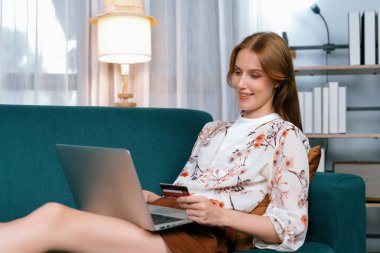 Genç mutlu kadın internetten alışveriş yaparak ürün satın alırken aynı zamanda internet üzerinden online ödeme sistemi ile çevrimiçi mağaza platformundan en yüksek siber güvenlik tarafından korunan ürünler sipariş ediyor.