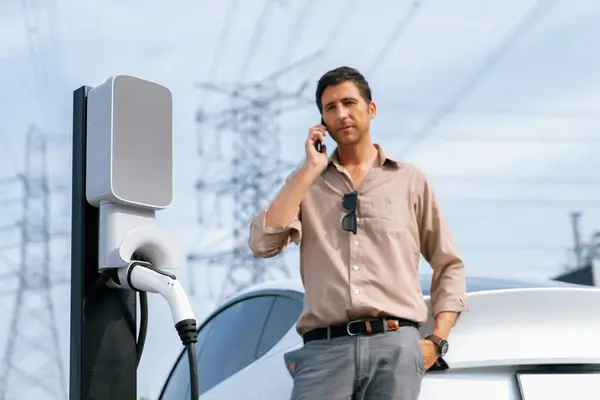 Man Talar Telefonen Medan Laddar Bilbatteri Laddstationen Ansluten Till Elnätet — Stockfoto
